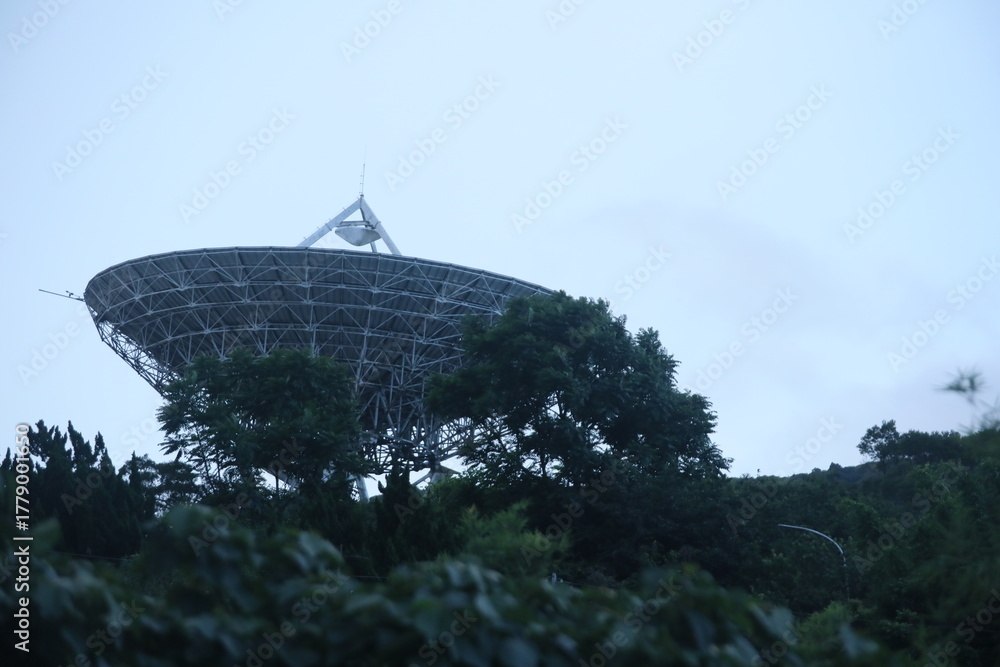 Fototapeta premium Taipei, Taiwan, - June 29th 2025 - A large, weathered satellite dish antenna at Yangmingshan Earth Station tilted towards the twilight sky.