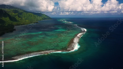 Aerial view of the vibrant turquoise waters meeting the dark blue ocean, separated by a reef with white waves, contrasting with the lush green coast, French Polynesia.