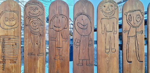 Children's drawings in the form of figures are burned into the fence in the kindergarten. Panorama.