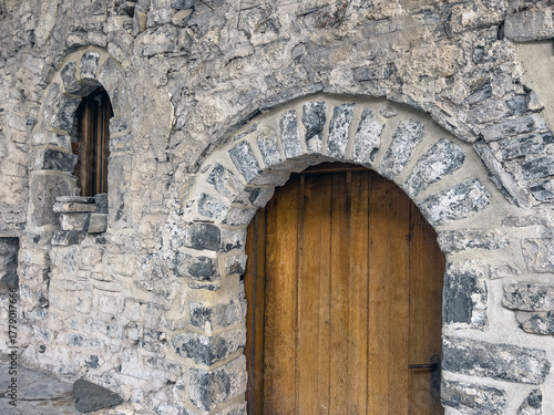 Rustic stone entrance with wooden door and arched window in vintage architecture