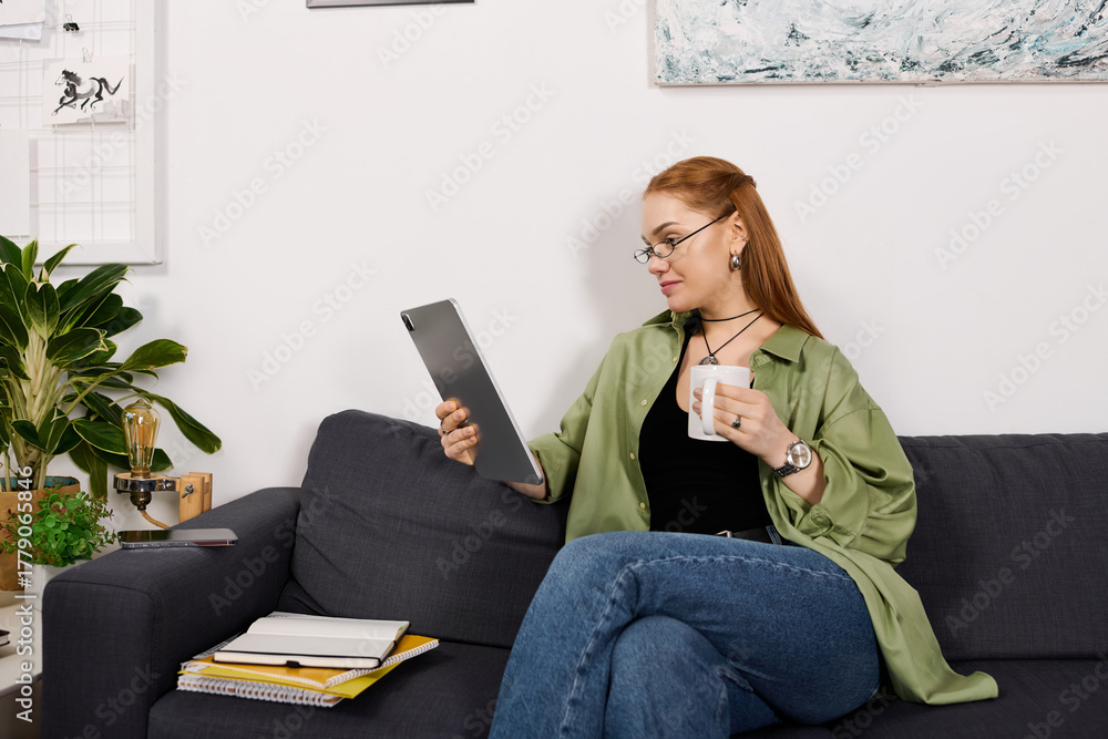 Obraz premium Cozy afternoon with a young woman enjoying her time at home reading on a tablet