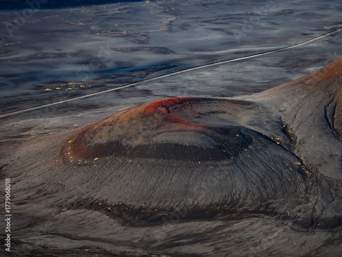 Bild auf Leinwand Aerial view of a volcanic cinder cone in Iceland's Highlands, with rusty red rim, dark ash, and a thin road in the distance