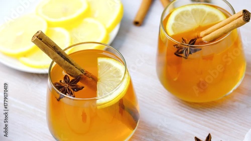 Two glasses warm spiced cider with cinnamon sticks, star anise, and lemon slices.