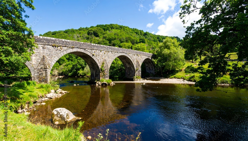Fototapeta premium Stone arch bridge over a river, lush green valley