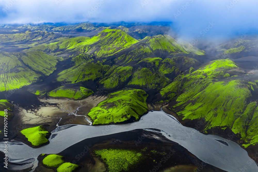 Fototapeta premium Aerial view of Landmannalaugar, Iceland, shows neon green moss on volcanic ridges and craters, black lava sands, and a braided glacial river under low clouds and diffuse light.