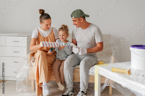Parents and daughter enjoy DIY home renovation. They share a tender moment teaching painting with a roller. Family teamwork and bonding.