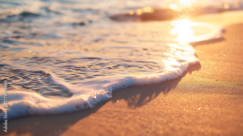 Fototapeta Naklejka Na Ścianę i Meble -  Gentle ocean wave washes onto a sandy beach at sunset with warm golden light