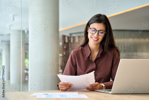 Cuadro en lienzo Smiling latin hispanic business woman working on laptop computer reading financial document report in office