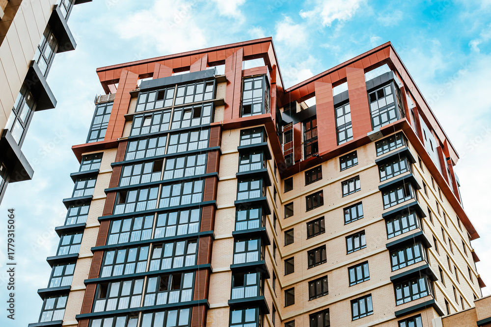 Fototapeta premium A modern residential building with distinctive angular lines, contrasting facades and windows, viewed from a low angle. New development
