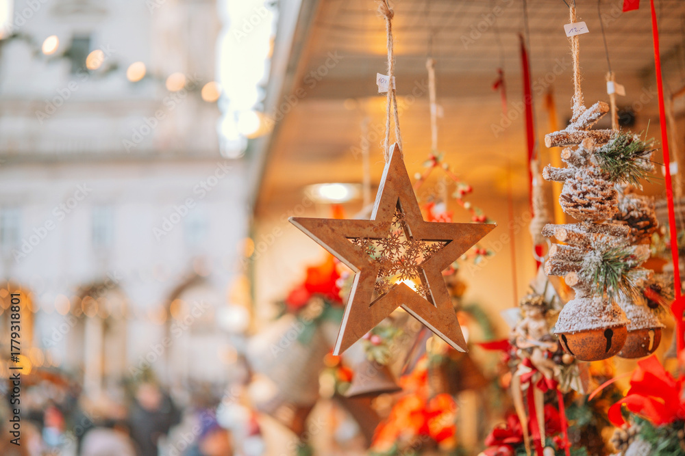 Fototapeta premium Wooden star ornament hanging with blurred festive winter market background and bokeh lights.