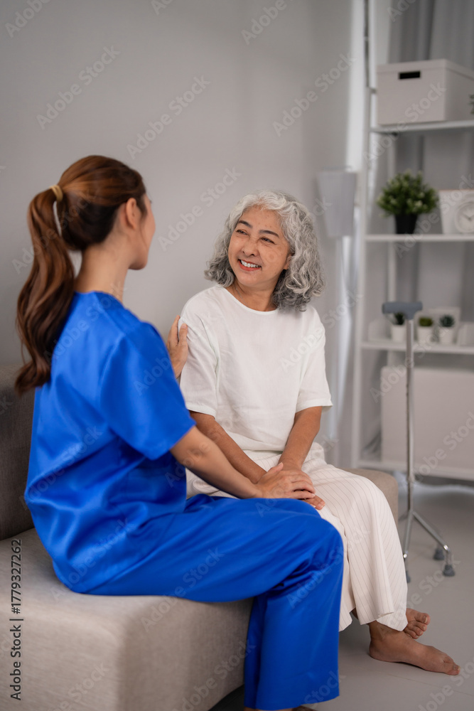 Obraz premium Asian young adult nurse provides compassionate home care support to smiling older Asian woman ensuring wellbeing and comfort in a bright living room environment