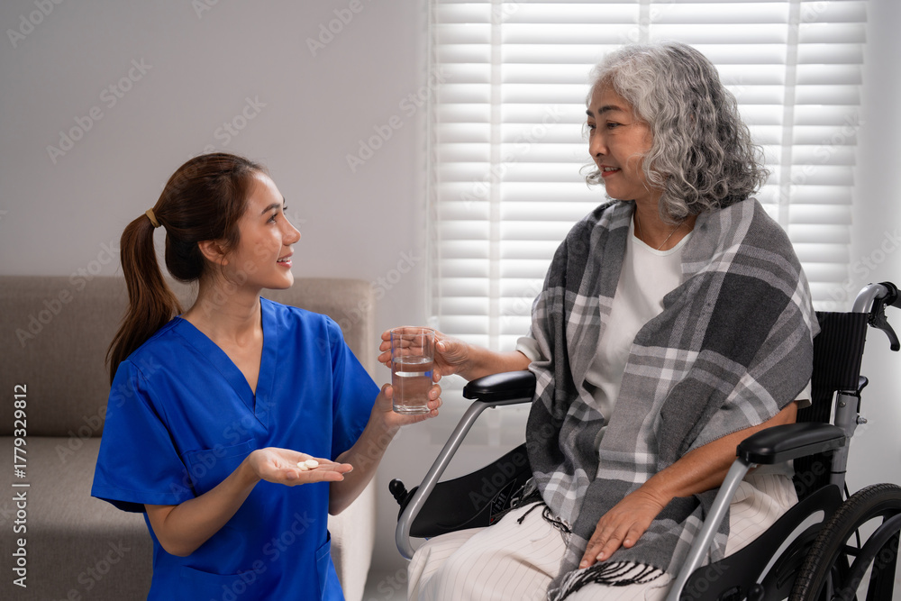 Fototapeta premium Asian young nurse giving medication water older adult woman wheelchair home care medical support wellness senior health assistance