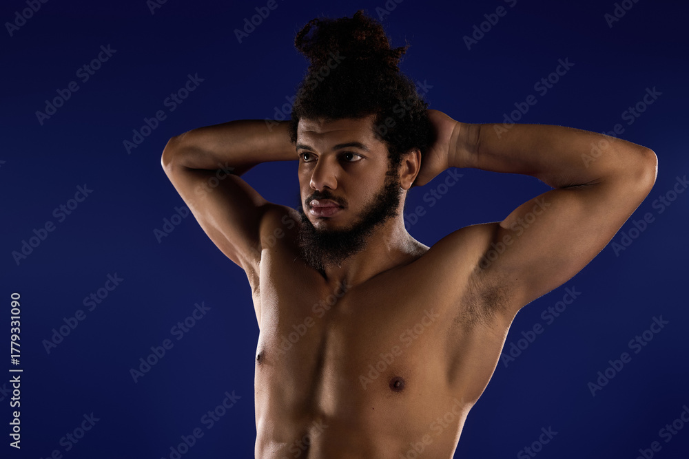 Fototapeta premium Athletic African American man demonstrates strength against a blue background