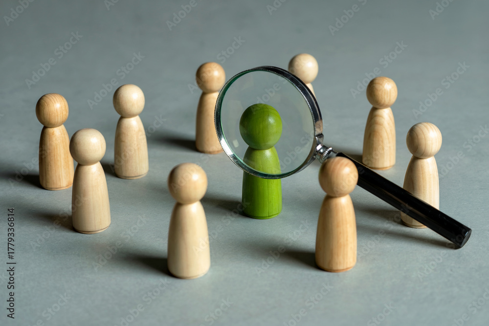 Obraz premium A Minimalist Business Concept Photograph Showing a Green Wooden Figure Under a Magnifying Glass for Talent Search