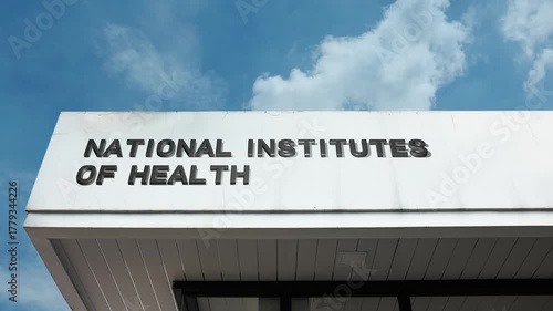 A National Institutes of Health word sign displayed on a large research facility under a clear blue sky, symbolizing medical science, public health, and biomedical research