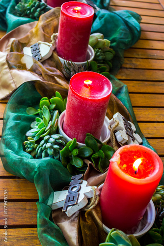 A summer Christmas Centre-piece, consisting of three lit candles, surrounded by succulents, wooden decorations and shiny bronze and green fabrics.