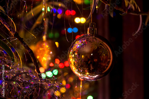 A golden ball, hanging from a Christmas tree, with the surrounding Christmas lights reflecting within