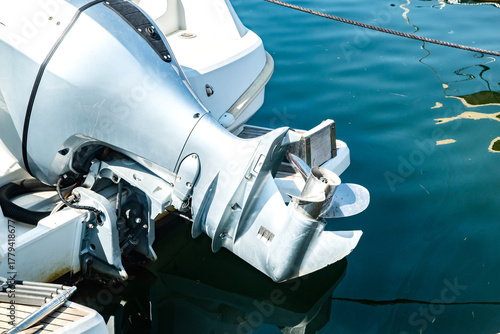 Fototapeta Naklejka Na Ścianę i Meble -  Close-up detail of outboard motor and propeller on docked marine boat, elevated above the water