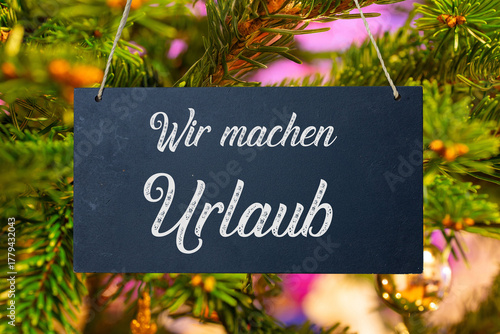 Betriebsferien an Weihnachten: Schild mit der Aufschrift WIR MACHEN URLAUB vor einem Weihnachtsbaum