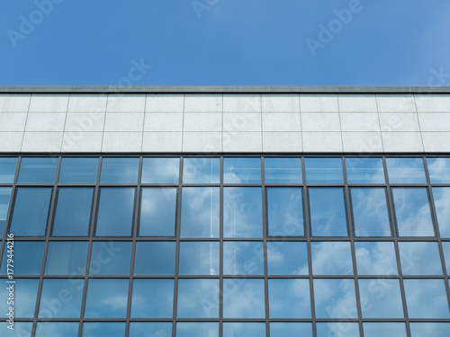 Modern building’s glass facade reflects blue sky and clouds