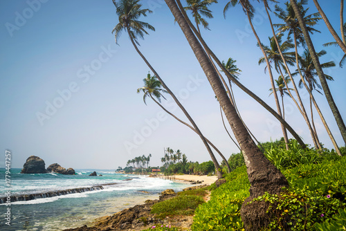 Topical beach with traditional fishing stilts in the distance on Koggala beach, Galle, Southern Province, Sri Lanka