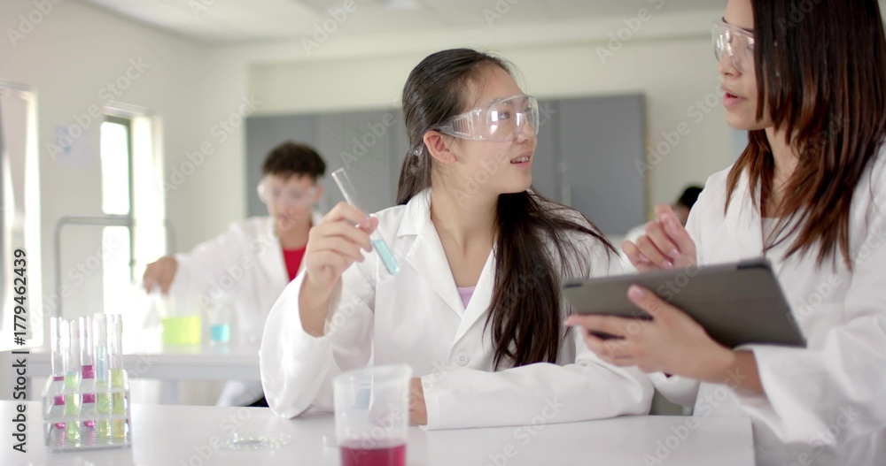 Obraz premium Analyzing blue solution Chinese girl wearing lab coat and goggles holding test tube in laboratory