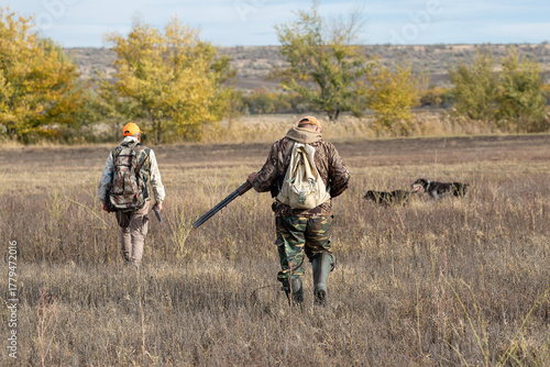 A hunters in camouflage clothing with a gun in his hands walks along the reeds.