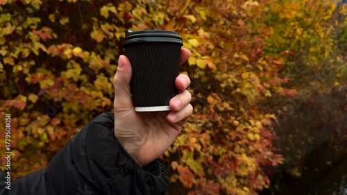 A black glass with a hot drink on the tipple against the background of yellow autumn trees.