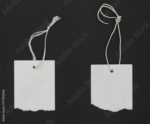 Torn white paper labels or tag with thread tie on black grunge paper background. White labels with copy space