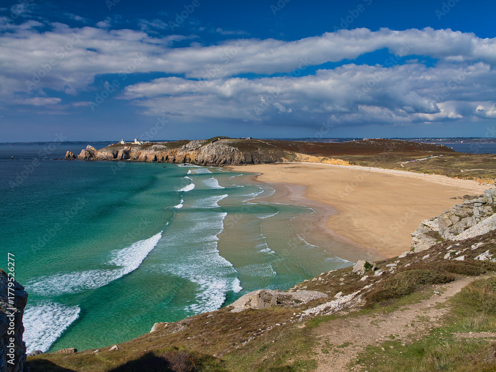 Obraz premium Turquoise waves sweep a wide golden beach beneath rugged cliffs at Pointe de Pen Hir on the Crozon Peninsula, Brittany, France, under a bright blue sky.