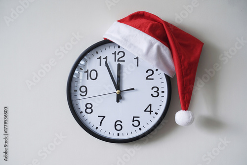 A Santa hat is on the office clock. The clock reads five to twelve.