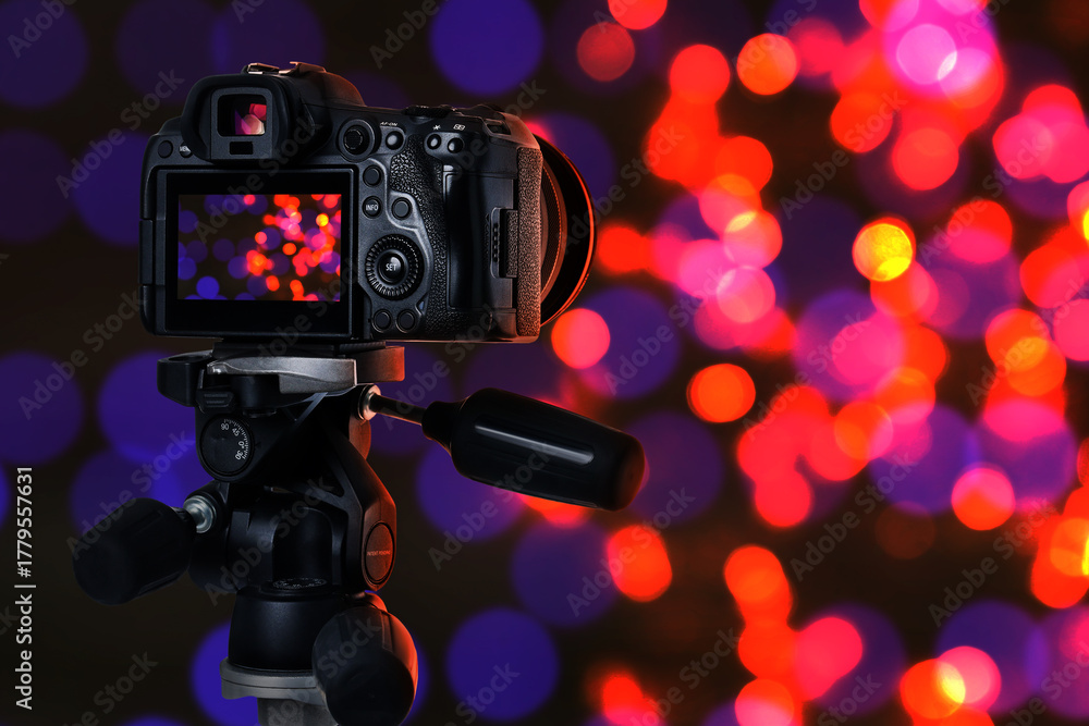 Fototapeta premium Professional camera against blurred lights on dark background, bokeh effect
