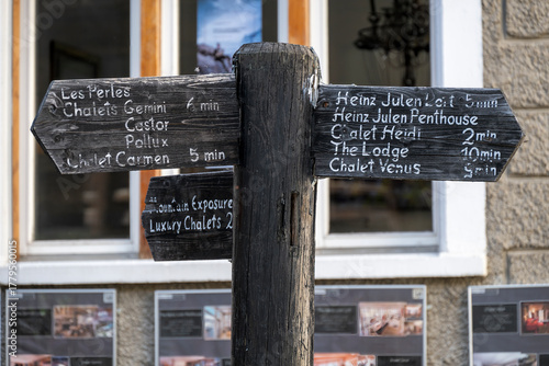 Weathered old dark wooden signpost with white inscriptions pointing  to the accommodations in Zermatt in the canton of Valais, Switzerland