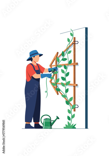 Gardener in overalls and hat tends to a climbing plant on a wooden trellis with a watering can nearby.