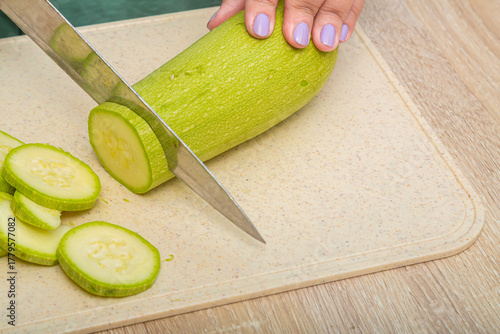 Young zucchini are cut with a knife on a wooden board on the table