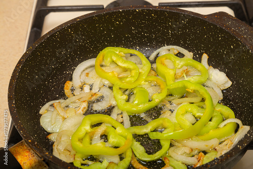 Yellow peppers cut with onions are fried in a frying pan in oil and spices