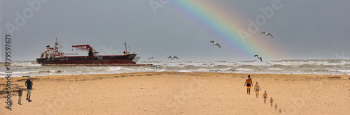 DREAM N°122 – Rainbow Beyond the Storm. Surreal and conceptual artwork depicting a cargo ship at sea under a gray sky, a bright rainbow emerging on the horizon, and figures walking on the beach.