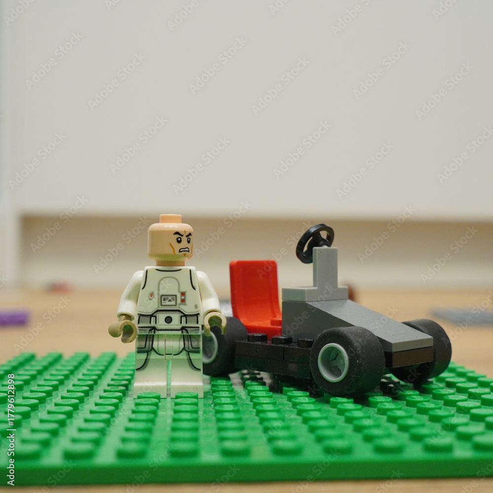 Fototapeta premium Lego minifigure and race car on a green baseplate, creative toy concept