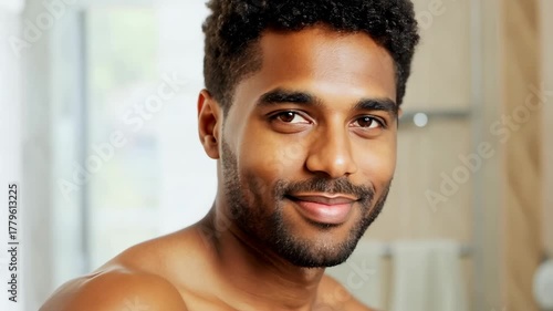 30 year old African American man in bathroom looking at camera and smiling. Body and skin care concept. Man in bathroom smiles brightly, embodying the results of his skin and body care.