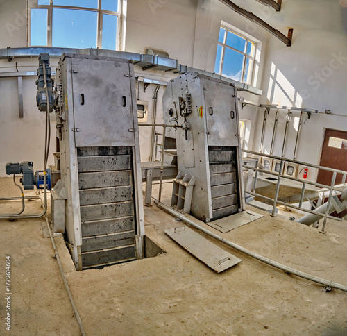 WWTP Coarse Mechanical Screening Hall. Two inclined mechanized bar screens with electric drives for removing large debris from wastewater.