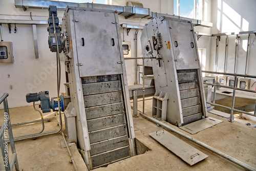 WWTP Coarse Mechanical Screening Hall. Two inclined mechanized bar screens with electric drives for removing large debris from wastewater.