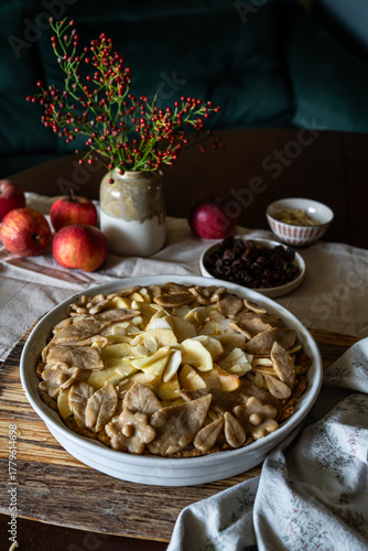 Unbaked homemade apple pie decorated with crust in baking form on rustic kitchen.