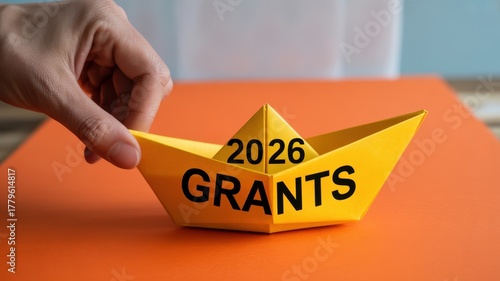 Hand holding yellow paper boat with 2026 grants written on it