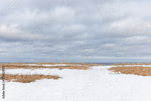 Fototapeta Naklejka Na Ścianę i Meble -  Open coastal landscape showing snowy patches on sandy terrain, calm distant sea