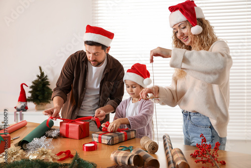Fotografía Happy family in Santa hats wrapping Christmas gifts at table indoors