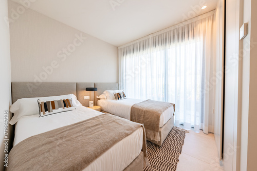 Two single beds in a bright bedroom with sheer curtains in holiday home 
