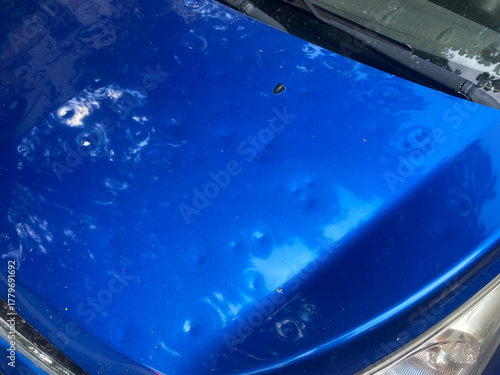 Pitted car hood after hailstorm. Close-up of dented automobile hood with hail damage. Multiple dimples and dents from hailstorm impact. Insurance, damage compensation.