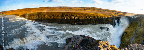 Gullfoss waterfall in Iceland showcases powerful cascades flowing into a canyon. Visitors admire the natural beauty from nearby viewpoints, especially during sunny weather.