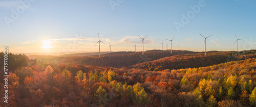 Wind turbines on the mountain between the vibrant fall forest at dusk