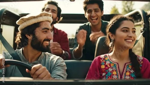 A group of four young adults laughing and enjoying a car ride with the top down on a sunny day outside